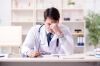 Un doctor estresado en su escritorio se frota los ojos, reflexionando sobre los complejos tipos de negligencia medica.
