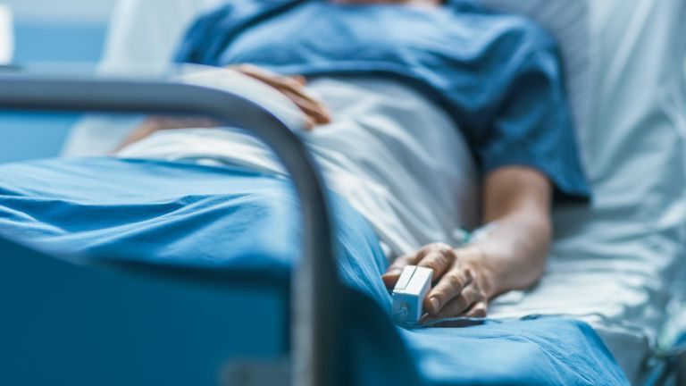 Un paciente acostado en la cama de un hospital, con su mano sujeta a una pinza de oxímetro, reflejando negligencia médica en hospitales.